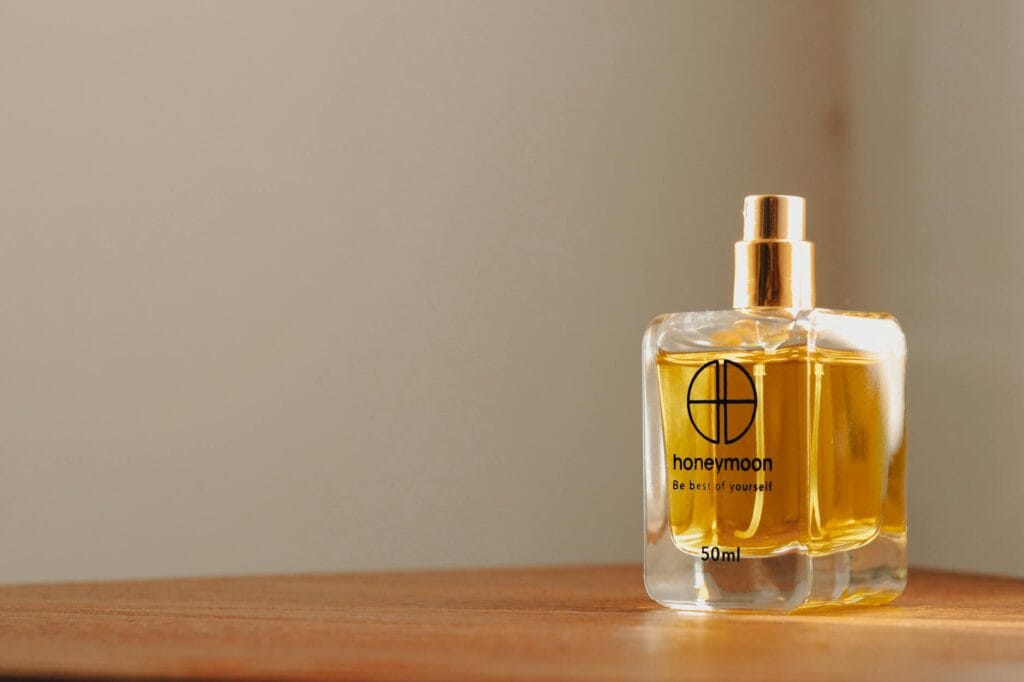 Perfume bottle and moisturizer on a wooden surface with text overlay: 15 Expert Tips to Make Your Perfume Last Longer All Day
