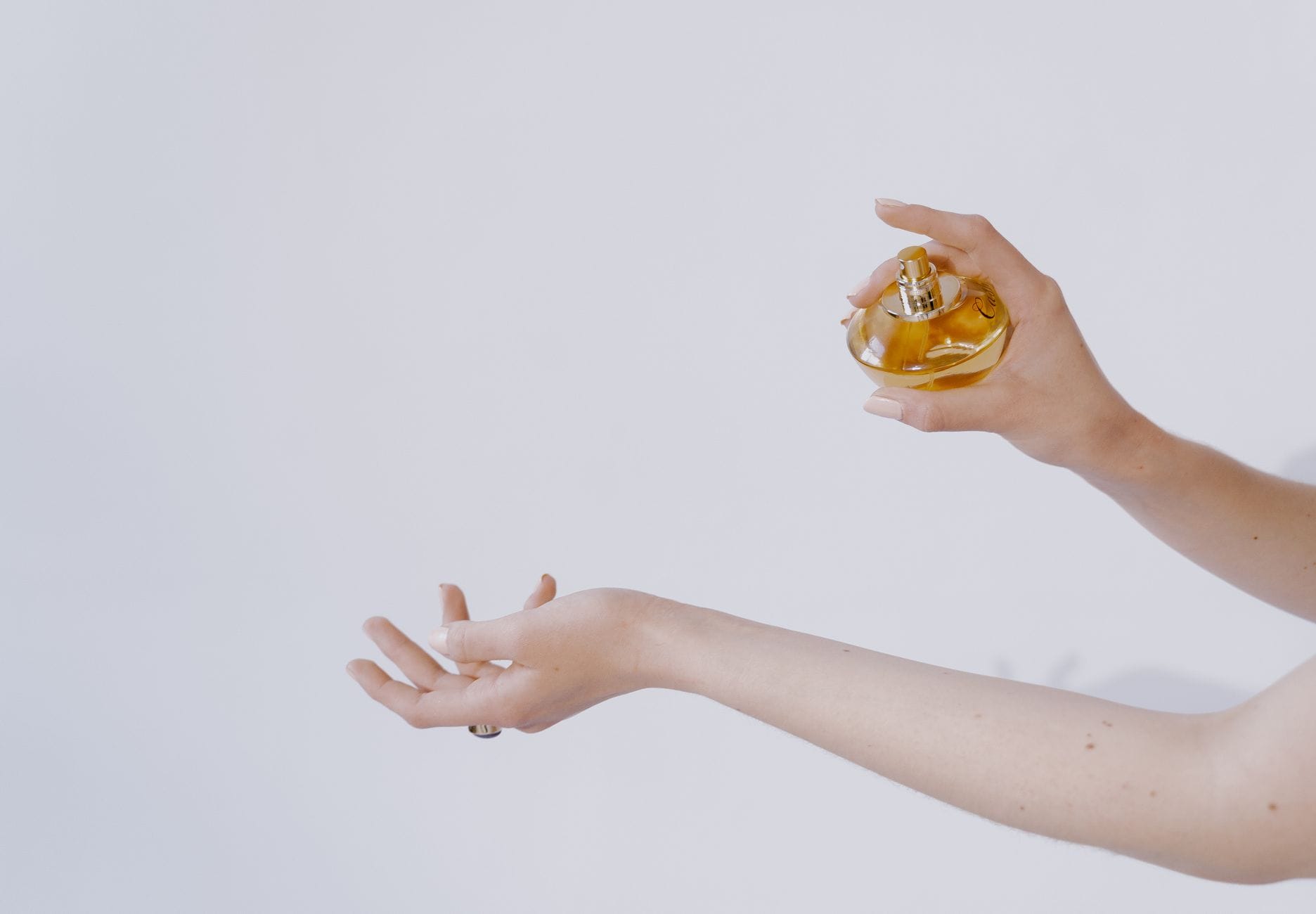 A woman applying perfume on her wrist with luxury fragrance bottles in the background, illustrating the art of perfume layering for beginners.