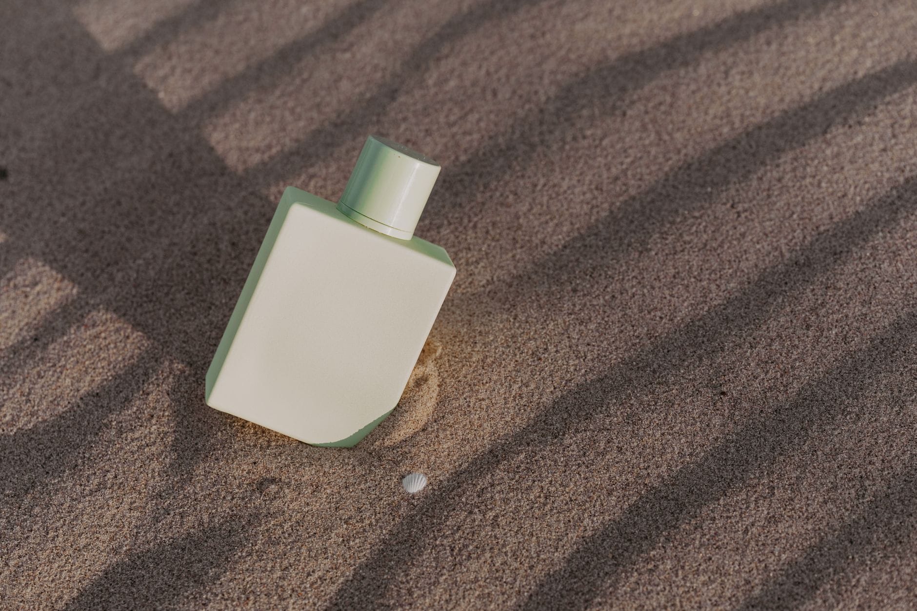 Elegant luxury summer perfume bottle resting on warm beach sand with tropical flowers under bright sunlight