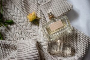 Elegant woman holding a fall perfume bottle in a cozy autumn setting with warm golden lighting and fall leaves.